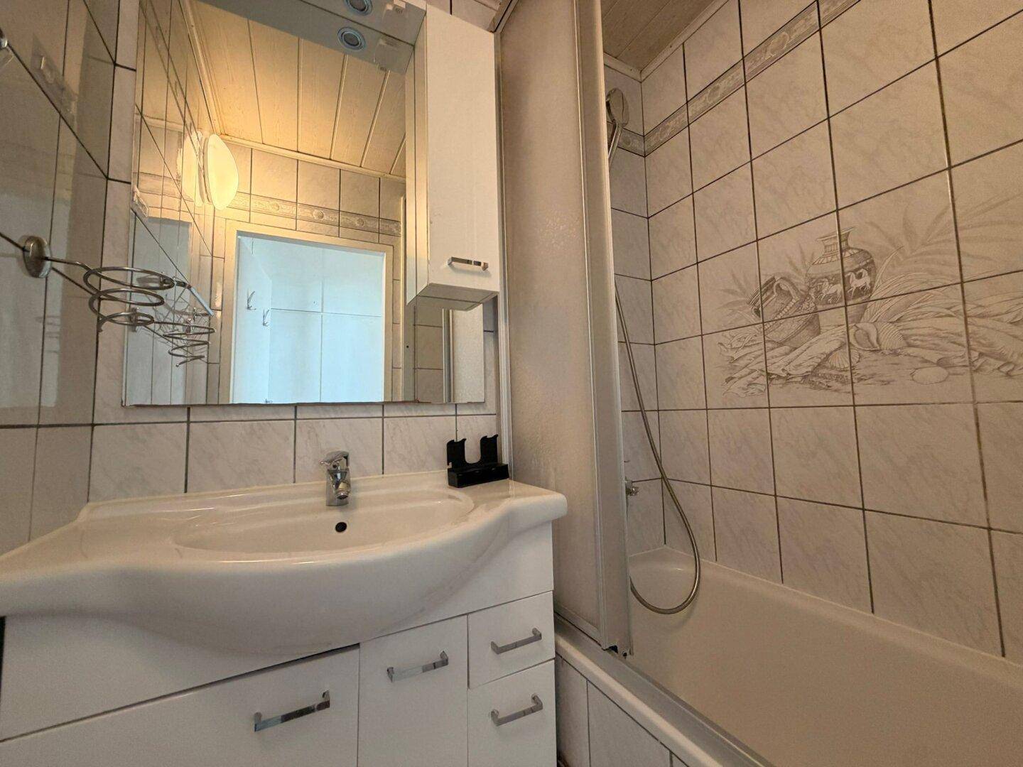 Badezimmer mit weiß gefliesten Wänden, Waschbecken, Spiegelschrank und Badewanne mit Duschvorhang.