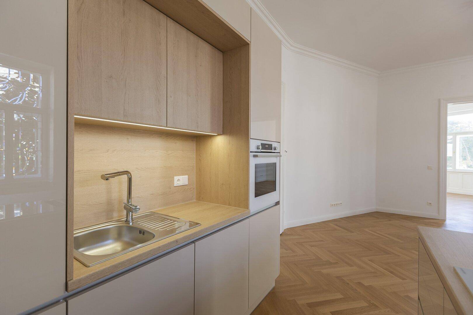 Detailansicht der modernen Küchenzeile mit Spüle, Backofen und Holz-Akzenten.