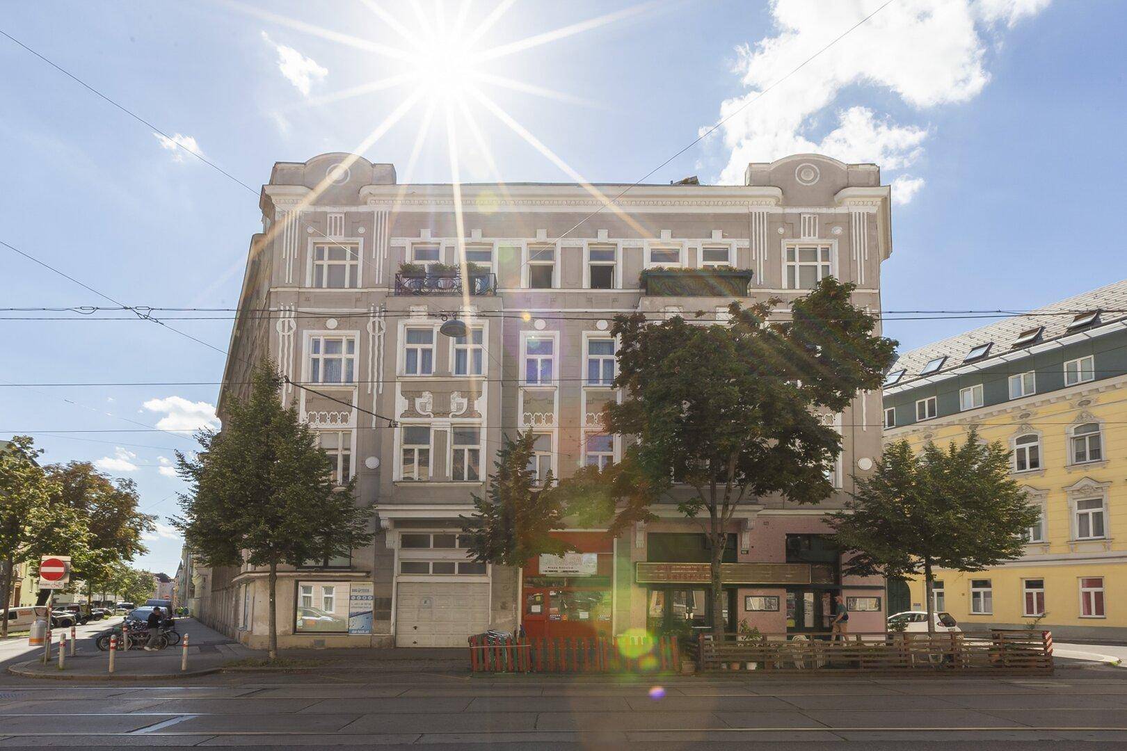 Historisches Mehrfamilienhaus mit Geschäften im Erdgeschoss an einem sonnigen Tag.