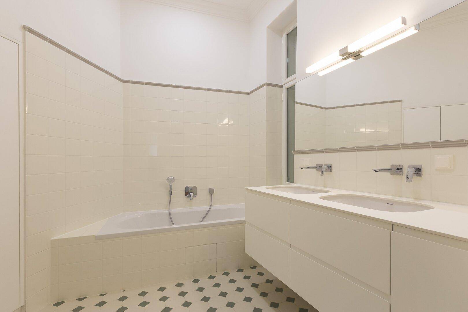 Modernes Badezimmer mit Doppelwaschbecken, Badewanne und gemusterten Bodenfliesen.