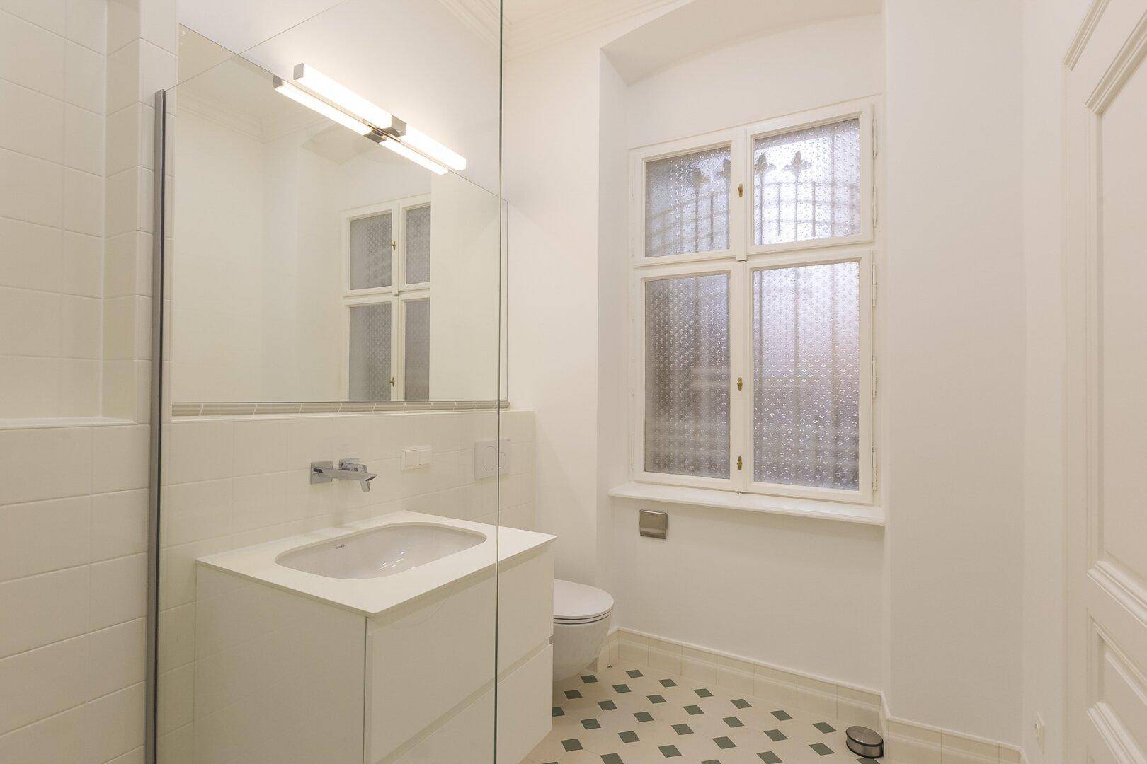 Helles Badezimmer mit Einzelwaschbecken, Toilette und Fenster für Tageslicht.