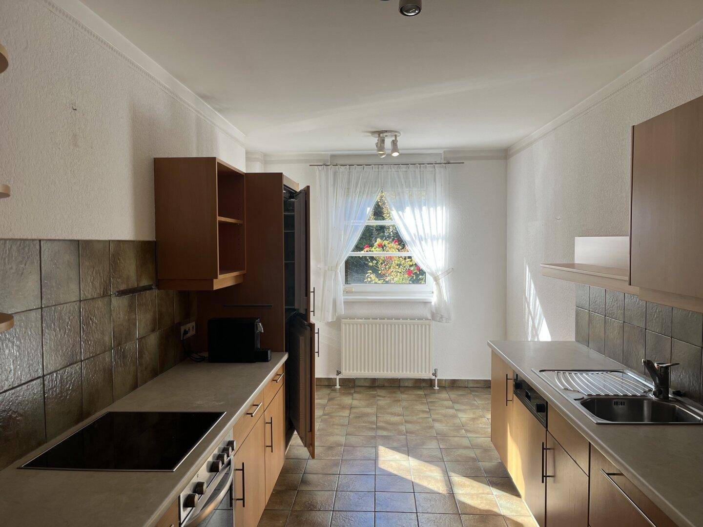 Funktionale Küche mit Holzschränken, gefliestem Boden und einem Fenster, das Tageslicht spendet.