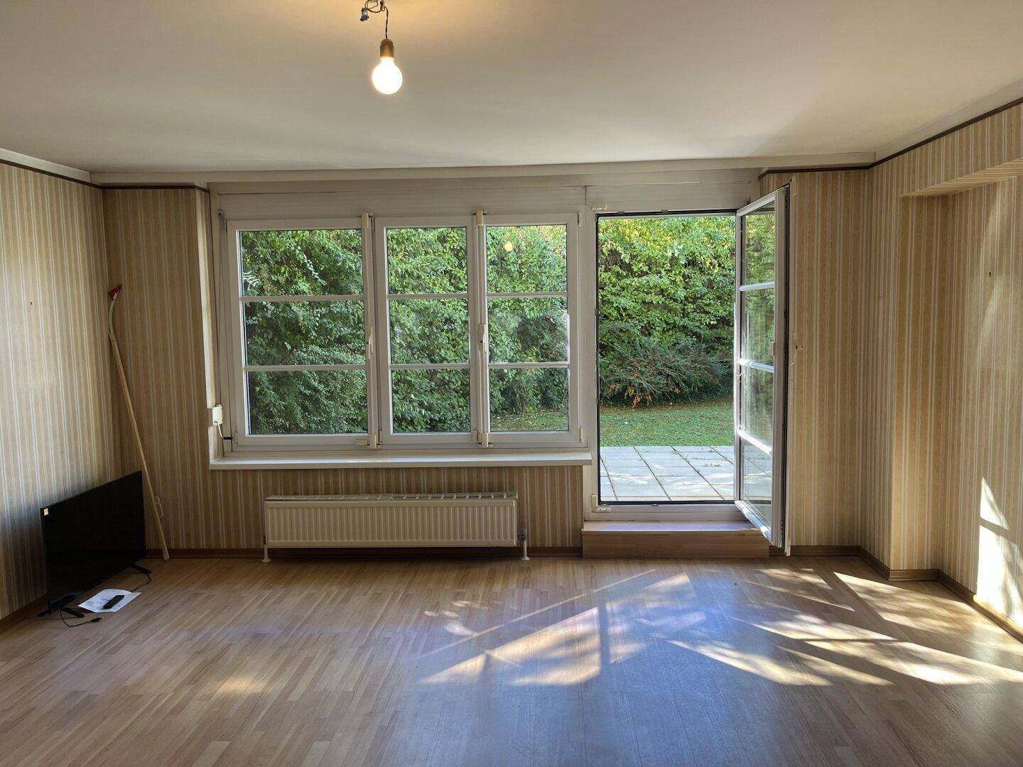 Helles Wohnzimmer mit Holzfußboden, gestreifter Tapete und direktem Zugang zur Terrasse.