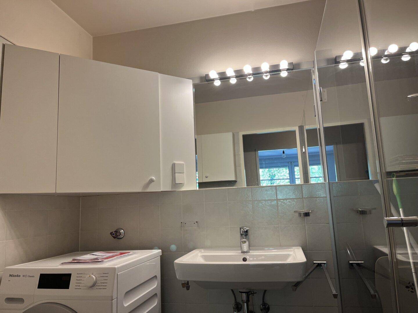 Modernes Badezimmer mit Waschbecken, Spiegelschrank, Dusche und Waschmaschine.