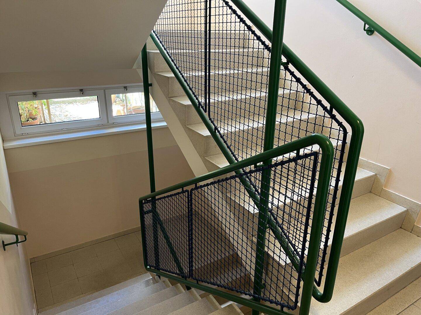 Treppenhaus mit grünen Geländern und gefliesten Stufen, das die verschiedenen Etagen verbindet.