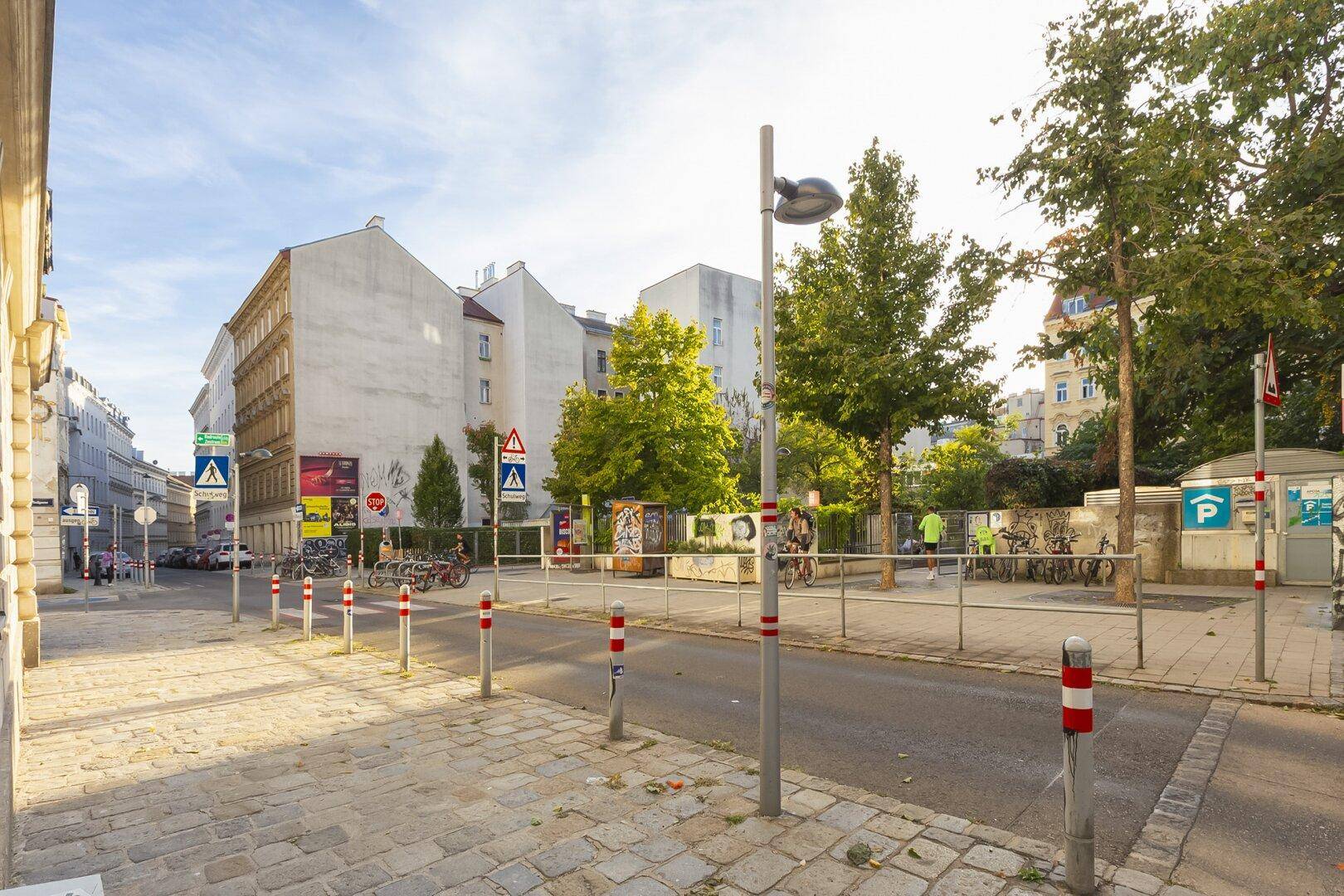Eine belebte Straße in der Stadt mit umliegenden Gebäuden und viel Grün.
