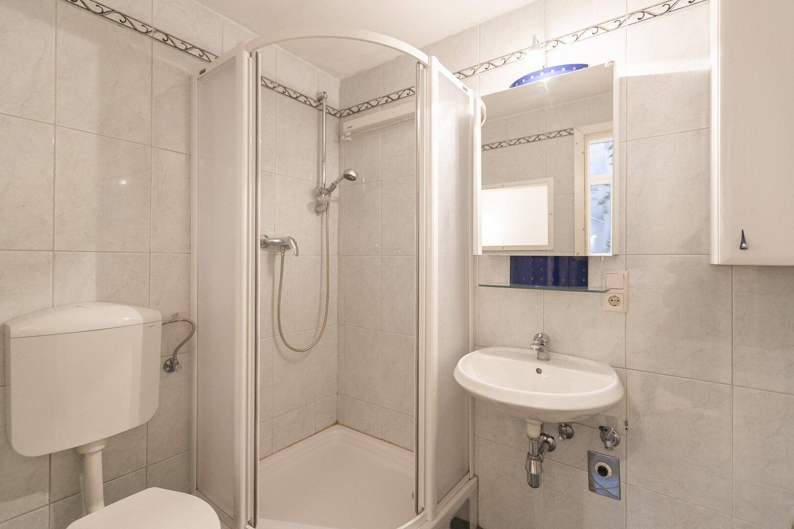 Funktionales Badezimmer mit Duschkabine, WC und Waschbecken, komplett gefliest in Weiß.