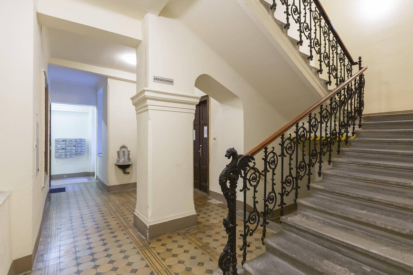 Repräsentatives Treppenhaus in einem Altbau mit schmiedeeisernem Geländer und gemustertem Fliesenboden.
