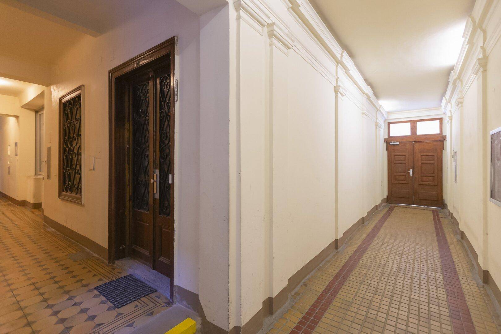 Langer Flur in einem Altbau mit gemustertem Fliesenboden und mehreren Holztüren.