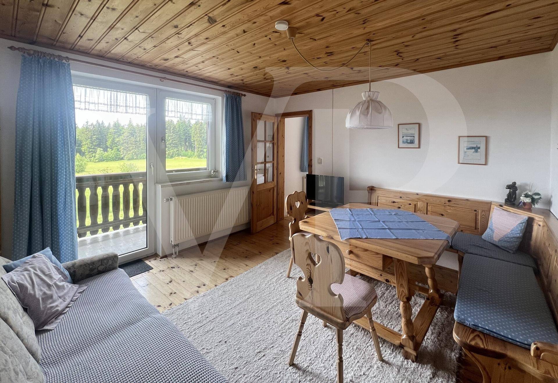 Heller Wohn-Essbereich mit Holzboden, Holzdecke und Balkonzugang mit Waldblick.