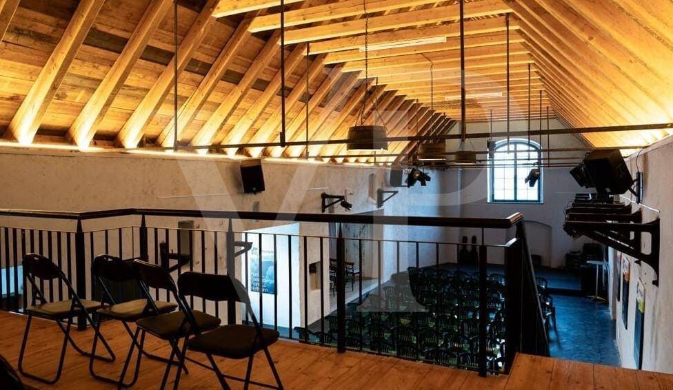 Blick von der Empore in den großen Saal, mit Holzdecke und Sitzgelegenheiten.