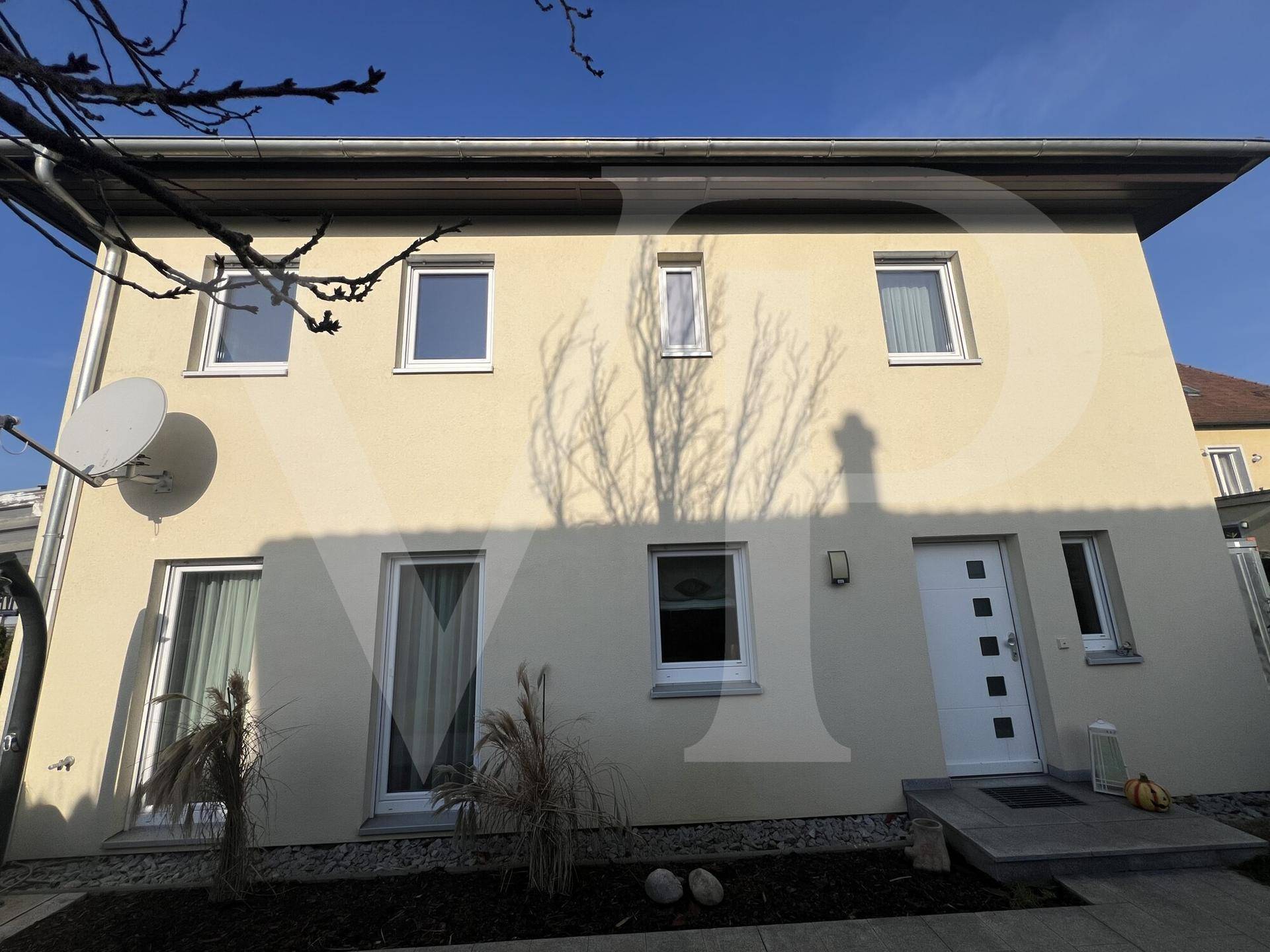 Vorderansicht des modernen Hauses mit heller Fassade, großen Fenstern und Eingangsbereich.