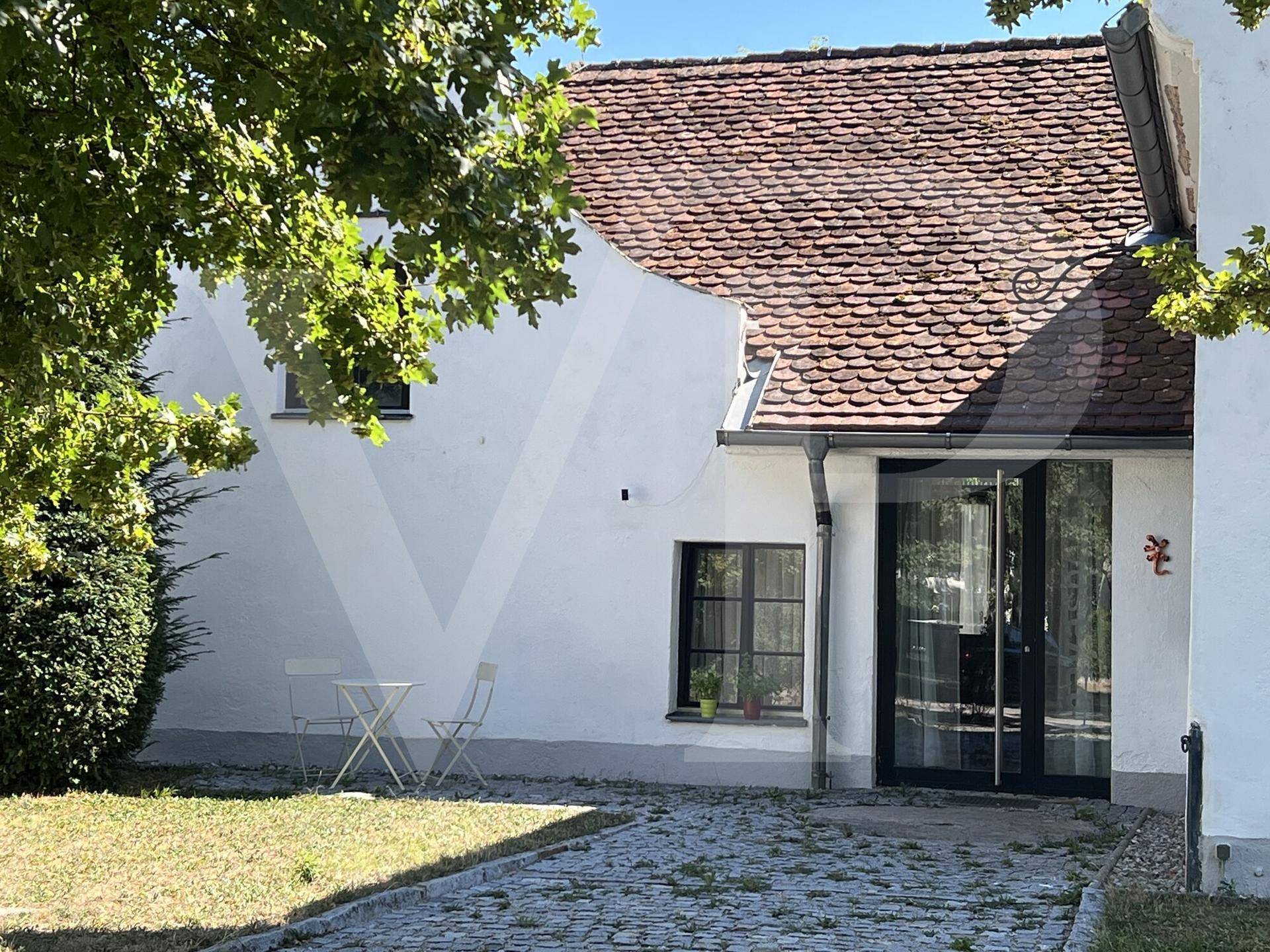 Fassade des Gebäudes mit gepflastertem Weg, grünem Rasen und Bäumen im Vordergrund.