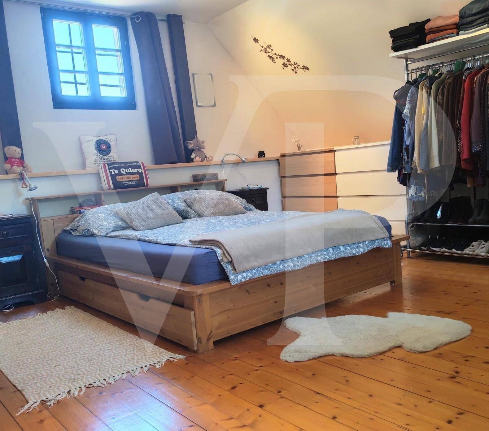 Schlafzimmer mit Holzbett, Kommode und offenem Kleiderschrank-System auf Holzfußboden.