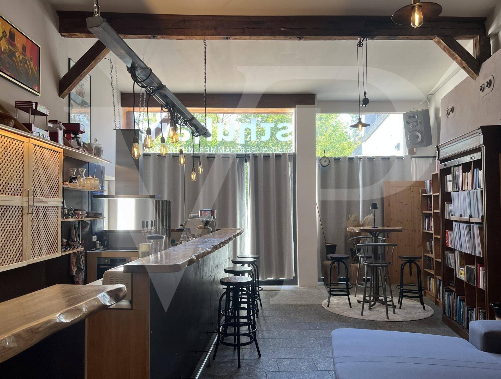 Bar-Bereich mit Holztresen, Barhockern und großen Fenstern, die viel Licht hereinlassen.