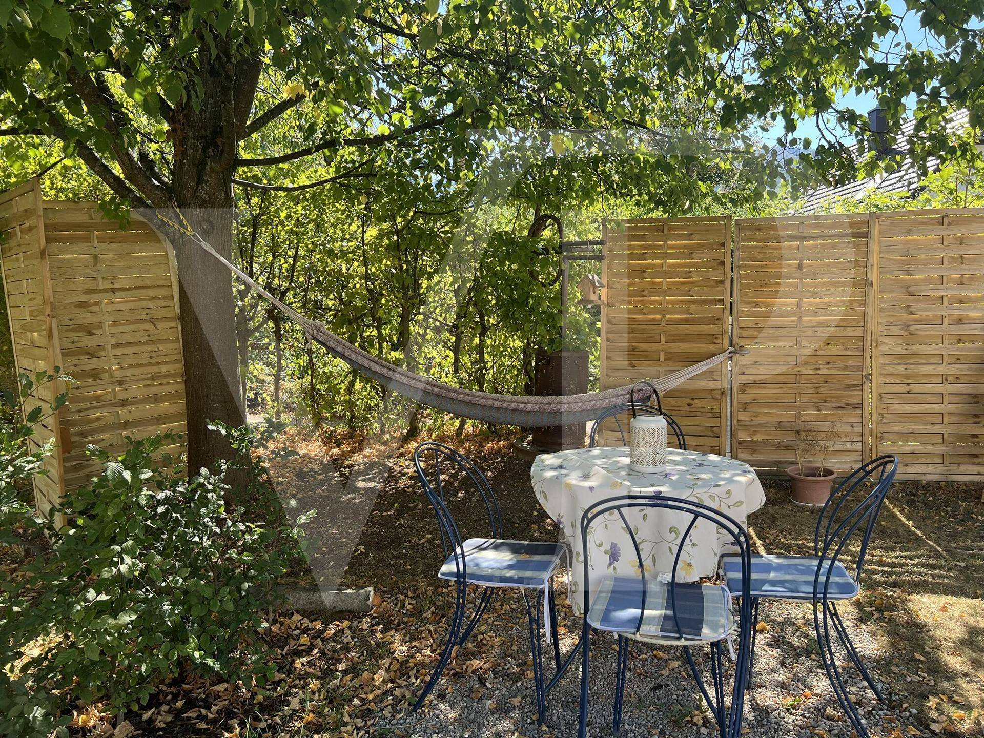Gemütlicher Gartenbereich mit Sitzgelegenheit, Hängematte und Sichtschutz unter einem großen Baum.