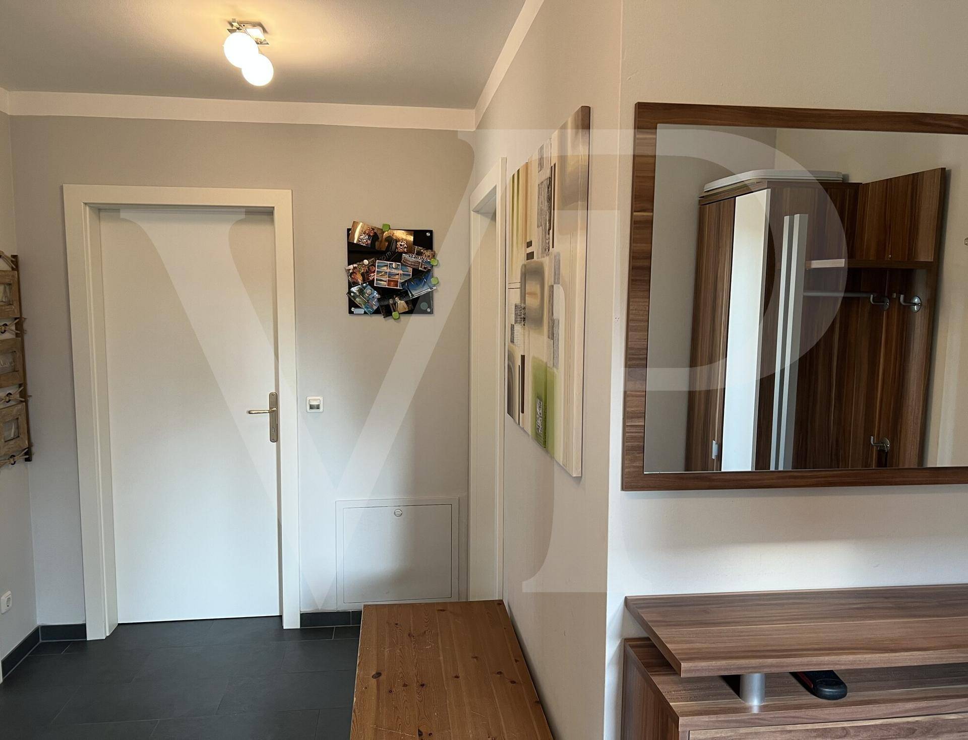 Eingangsbereich mit dunklen Fliesen, Holzmöbeln und einem Spiegel.