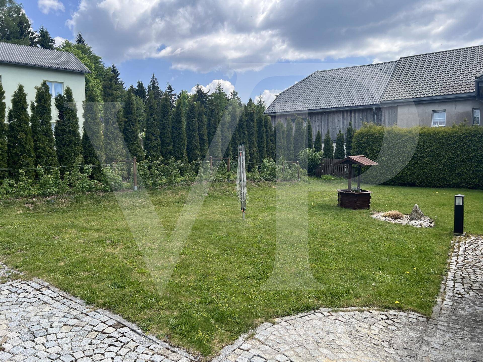 Gepflegter Gartenbereich mit Rasenfläche, Zierbrunnen und hohen Hecken als Sichtschutz.
