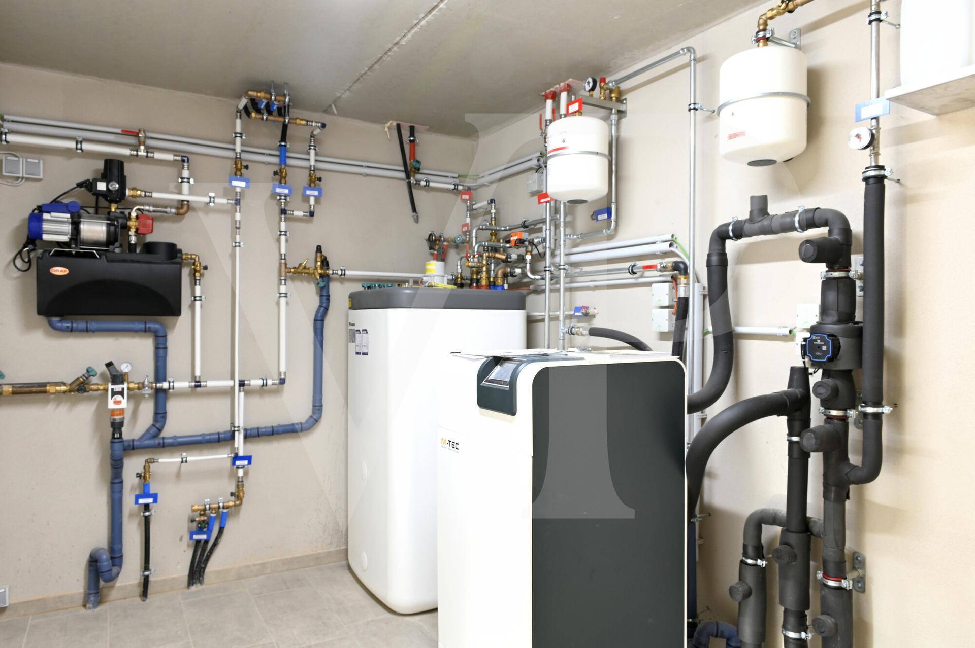 Technikraum mit Heizungsanlage, Warmwasserspeicher und komplexer Rohrinstallation.