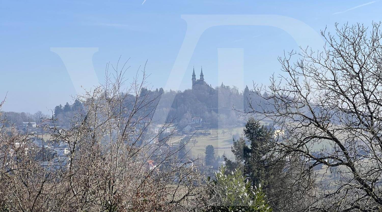 Panoramablick auf eine Kirche auf einem Hügel in der Ferne, umgeben von ländlicher Landschaft.