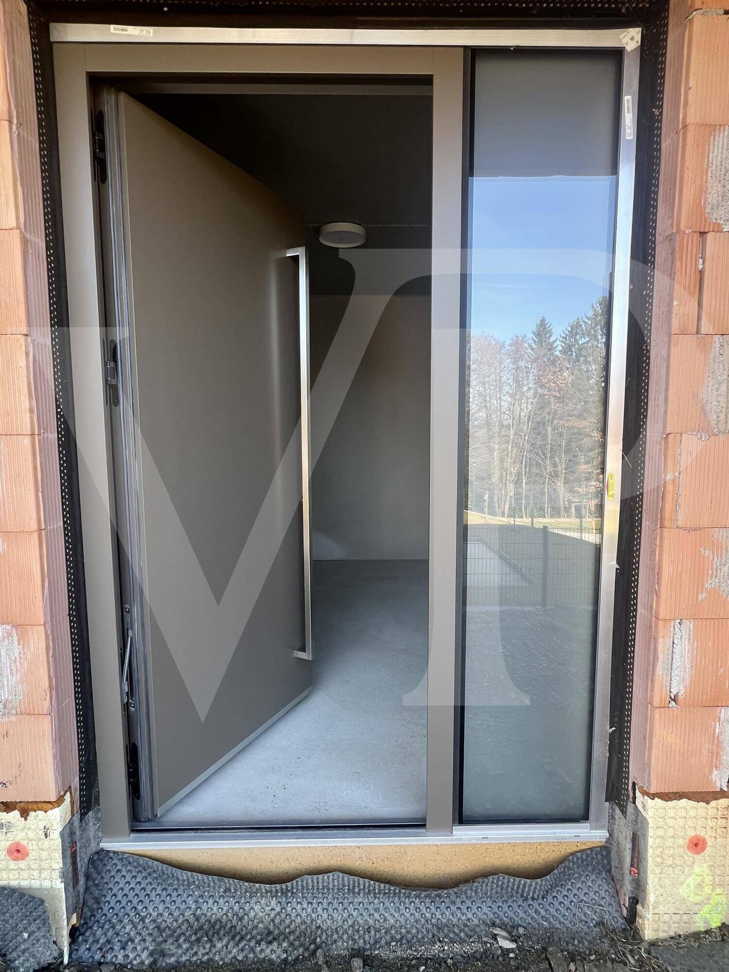 Moderner Hauseingang mit großer Tür und seitlichem Glaselement im Rohbau.