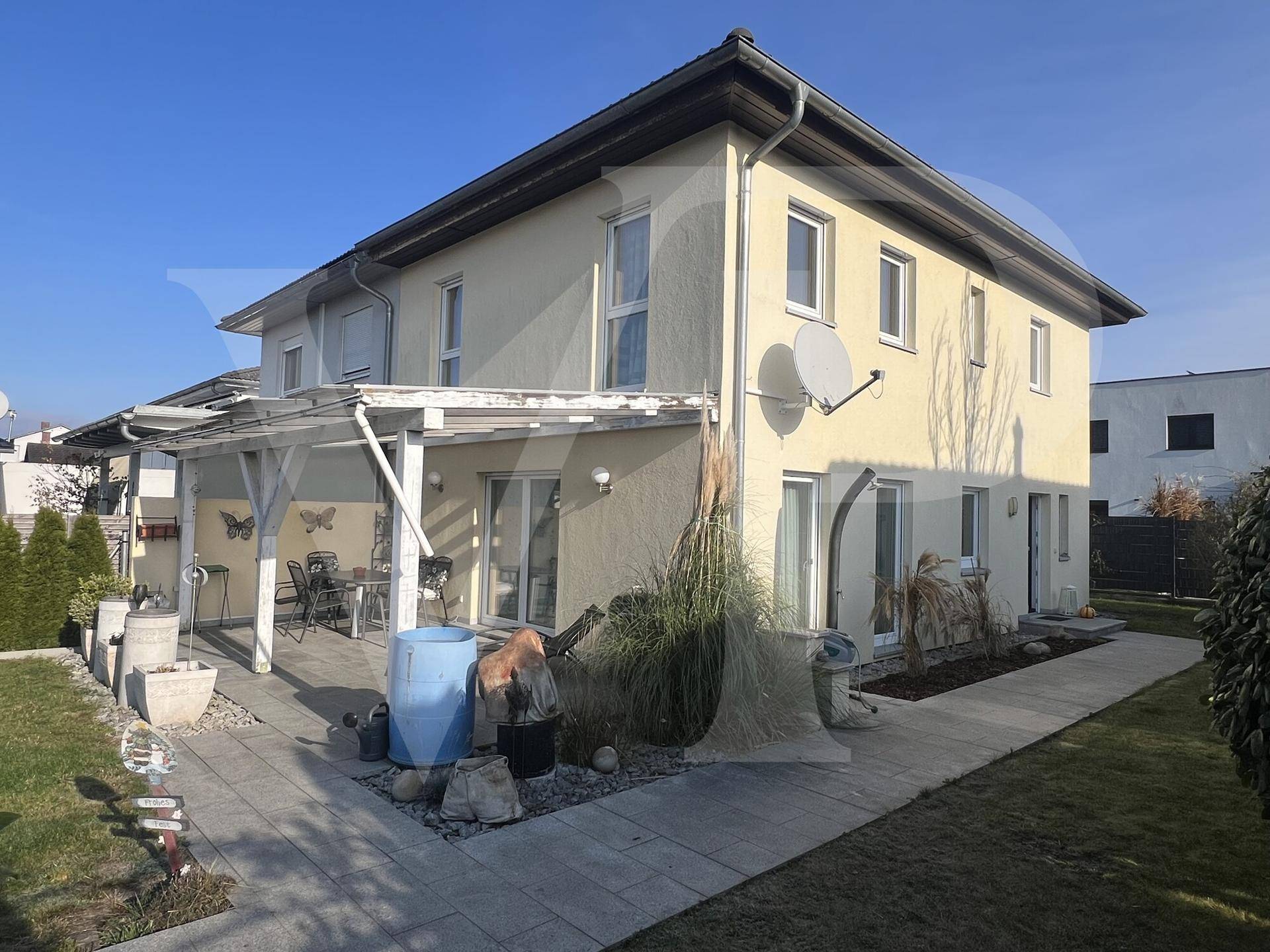 Rückansicht des Hauses mit gepflasterter Terrasse, Pergola und gepflegtem Gartenbereich.