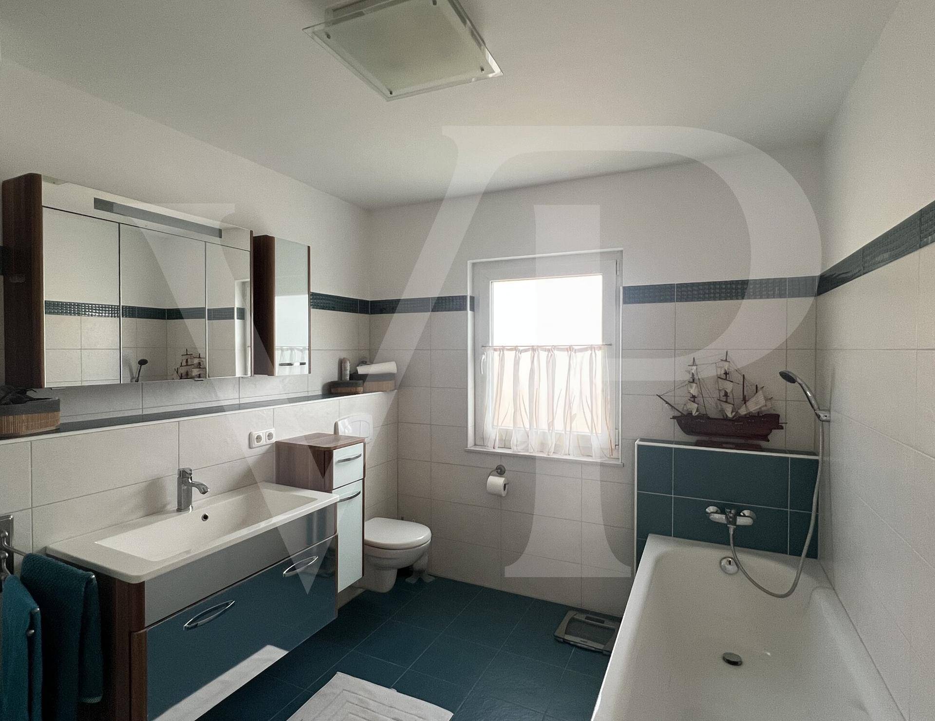 Badezimmer mit Badewanne, Waschbecken, WC und Fenster für Tageslicht.