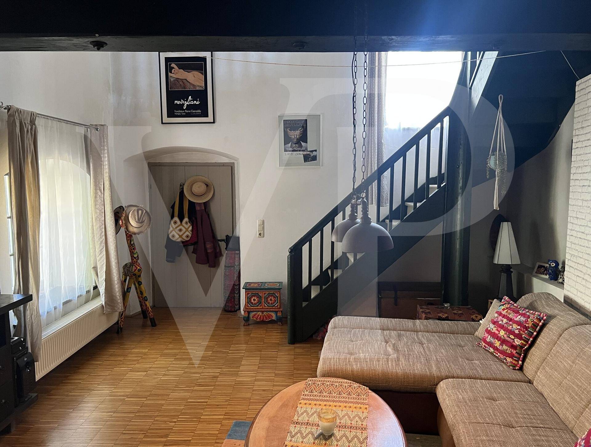 Wohnzimmer mit bequemer Couch, rundem Couchtisch und einer Holztreppe, die nach oben führt.