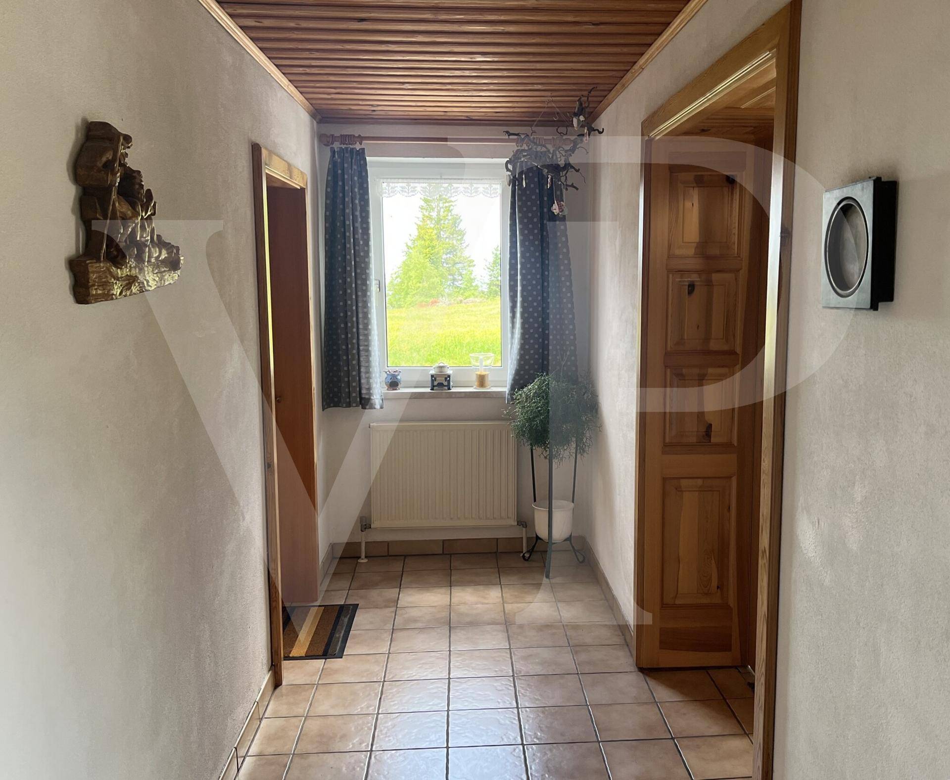 Heller Flur mit Fliesenboden, Holzdecke und Fenster mit Blick ins Grüne.