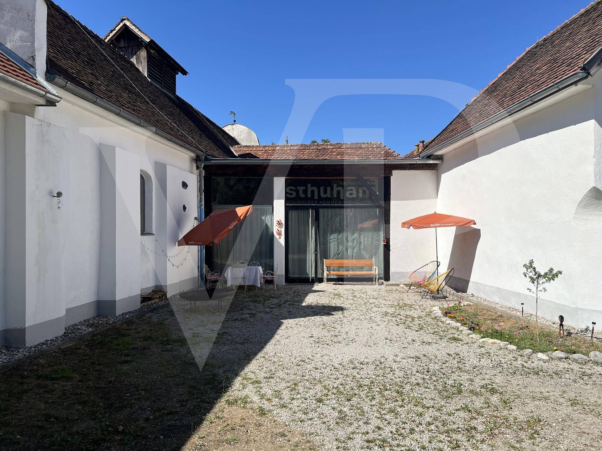 Innenhof mit Kiesfläche, moderner Glasfassade und gemütlicher Sitzgelegenheit unter Sonnenschirmen.