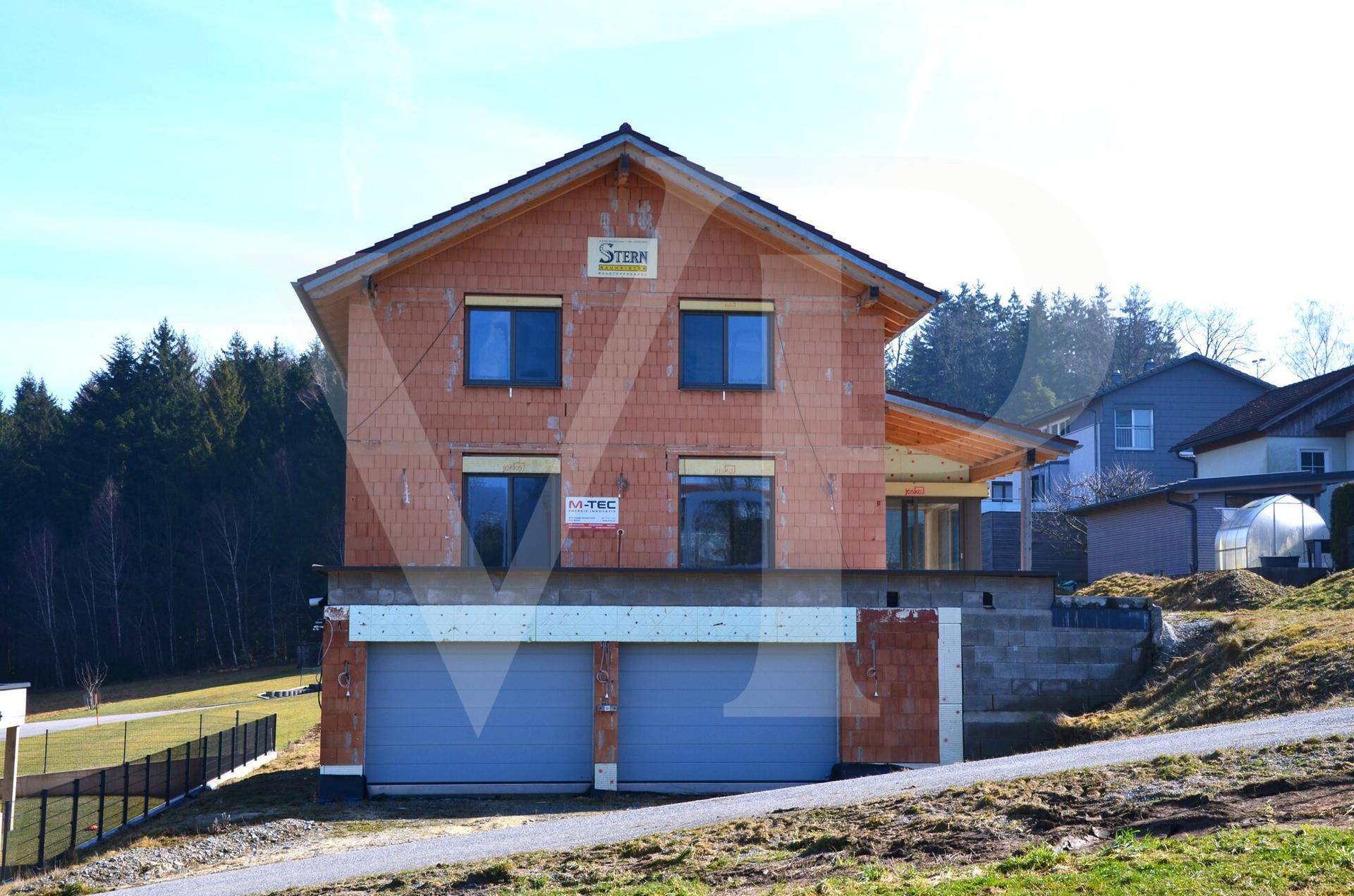 Rohbau eines Einfamilienhauses mit Doppelgarage und Blick auf den Wald.