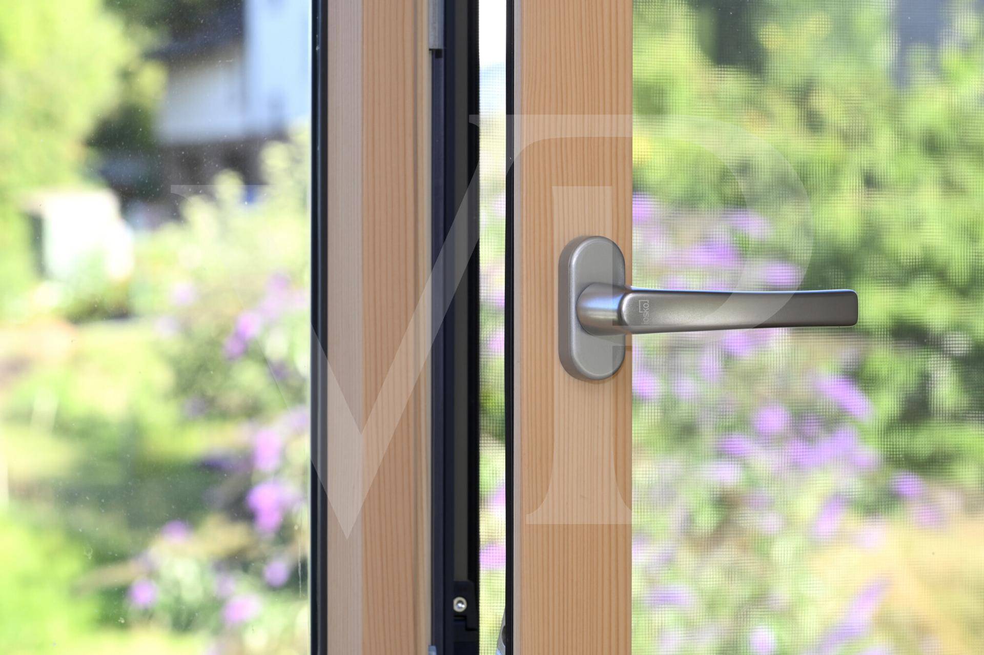 Detailaufnahme eines modernen Fenstergriffs mit Blick auf blühende Pflanzen.
