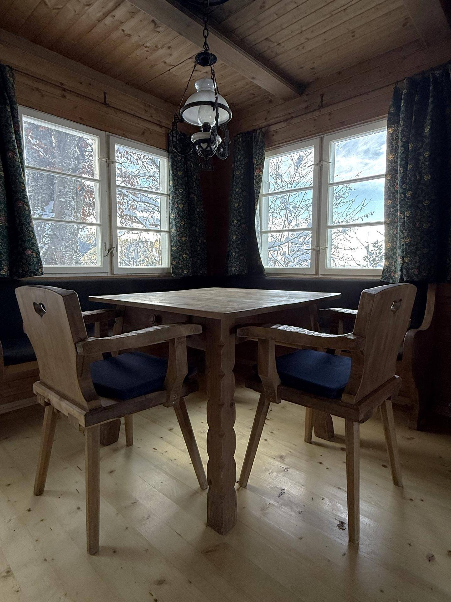 Rustikaler Essbereich mit Holztisch und Stühlen, umgeben von Holztäfelung und großen Fenstern.