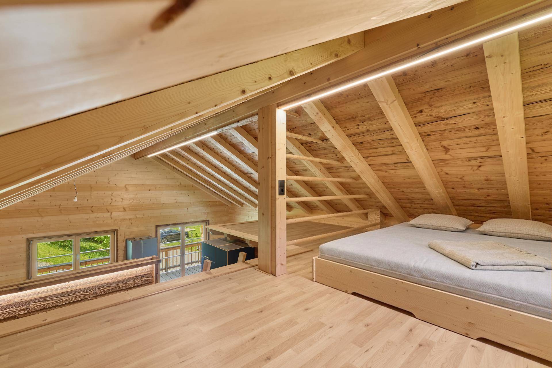 Gemütliches Schlafzimmer im Dachgeschoss eines Holzchalets mit Holzbalken und Doppelbett.