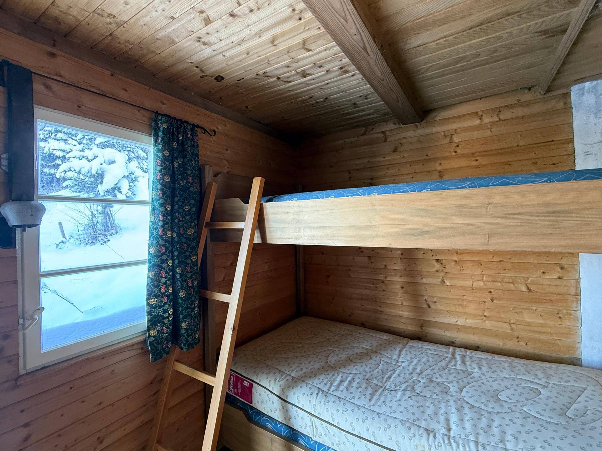 Gemütliches Schlafzimmer mit Etagenbett und Holztäfelung, Blick auf die verschneite Landschaft.