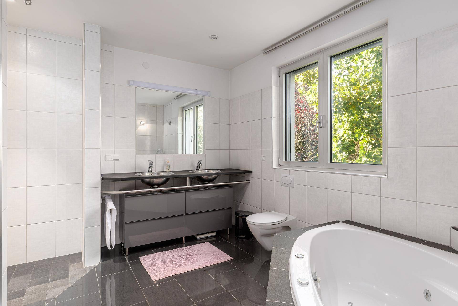 Modernes Badezimmer mit Doppelwaschbecken, Badewanne und großem Fenster für Tageslicht.