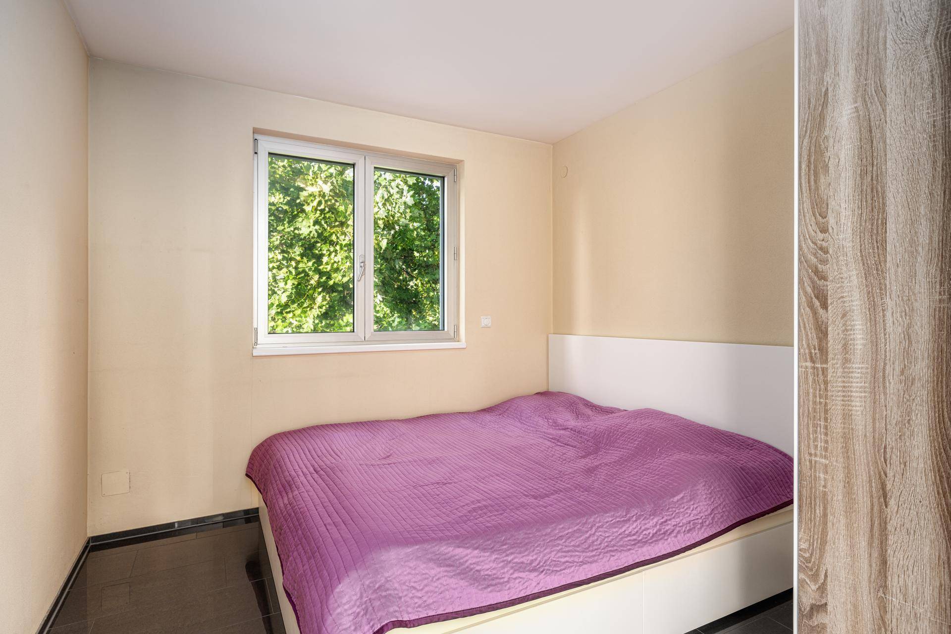 Helles Schlafzimmer mit Doppelbett und Fenster, das einen Blick ins Grüne bietet.