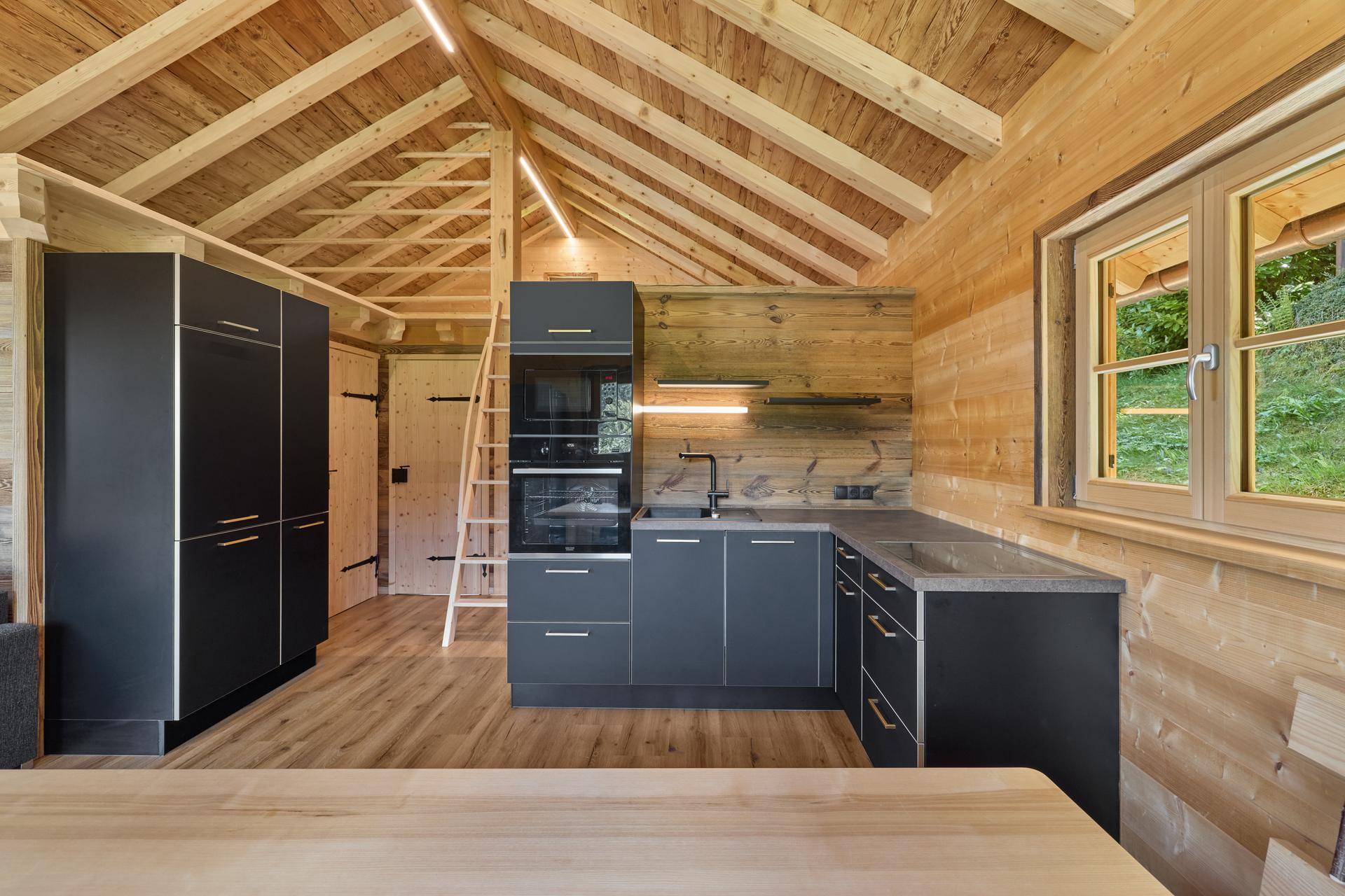Gut ausgestattete Küche in einem Holzchalet mit dunklen Fronten und Holzwänden.