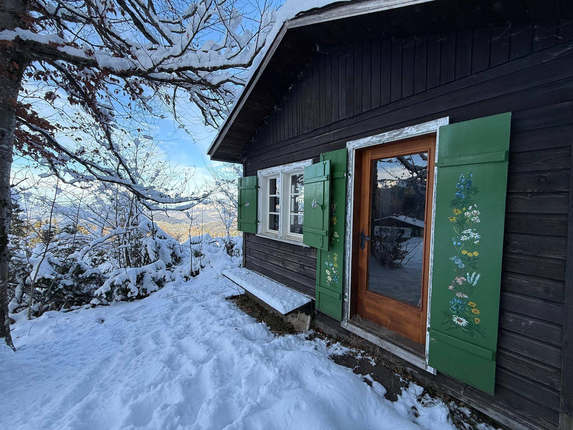 Rustikale Holzhütte mit grünen Fensterläden und verschneiter Umgebung in den Bergen.
