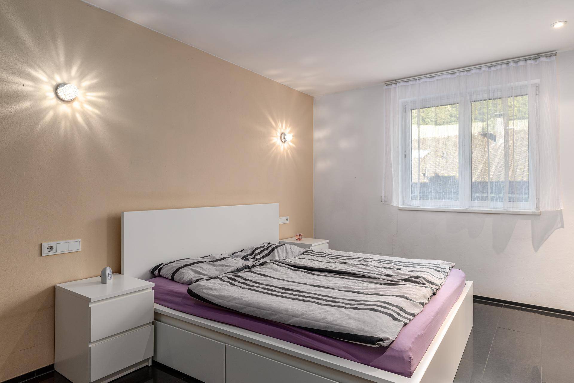 Helles Schlafzimmer mit Doppelbett, Nachttischen und Fenster mit Blick ins Grüne.
