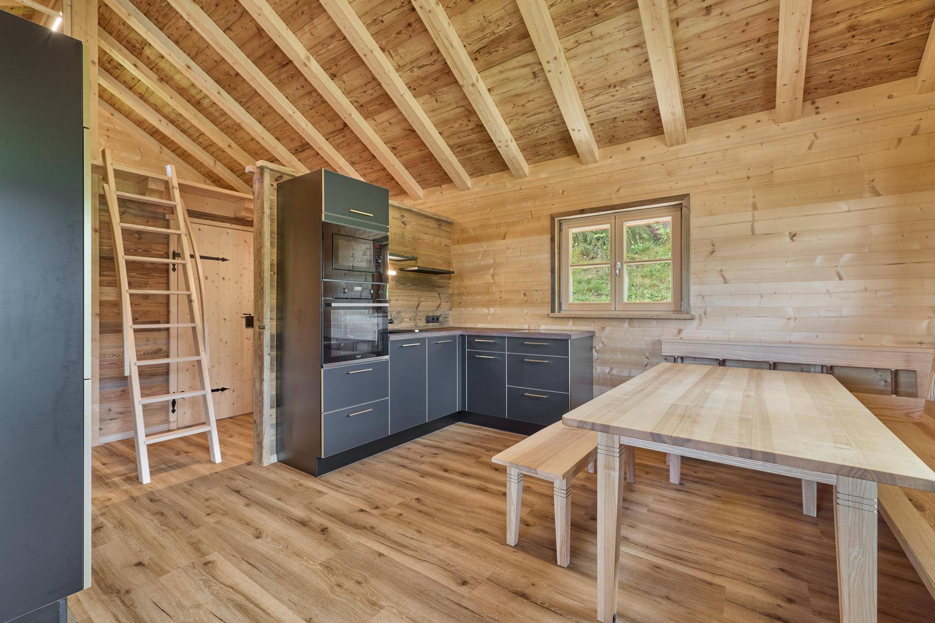 Moderne Küche in einem Holzchalet mit dunklen Schränken und Holzbalkendecke.