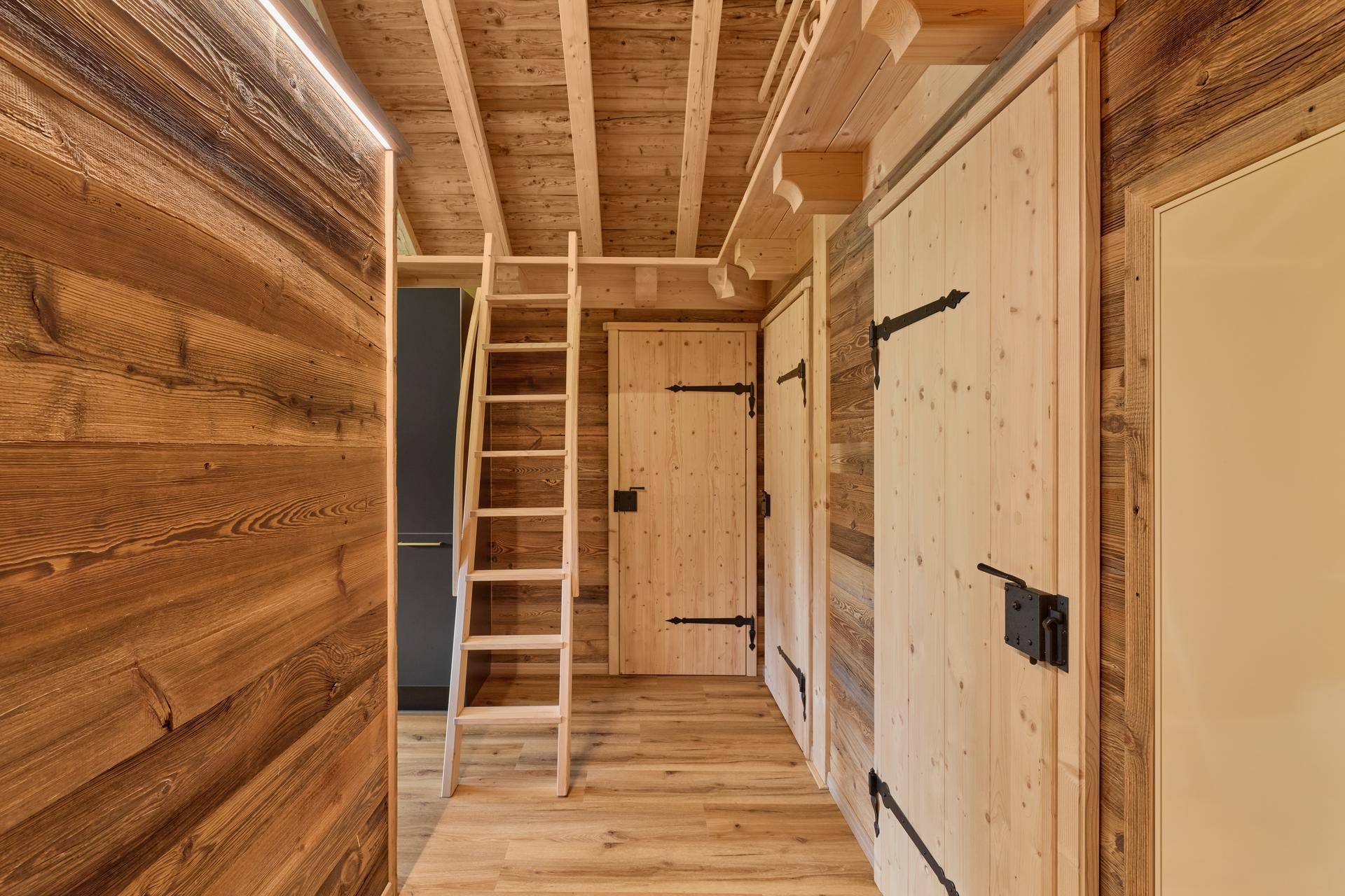 Flur in einem Holzchalet mit Holzwänden, rustikalen Türen und Leiter zum Dachboden.