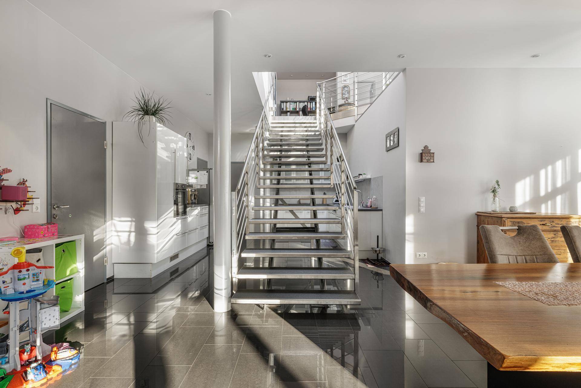 Heller offener Bereich mit Küche, Essplatz und moderner Treppe als zentrales Element des Raumes.