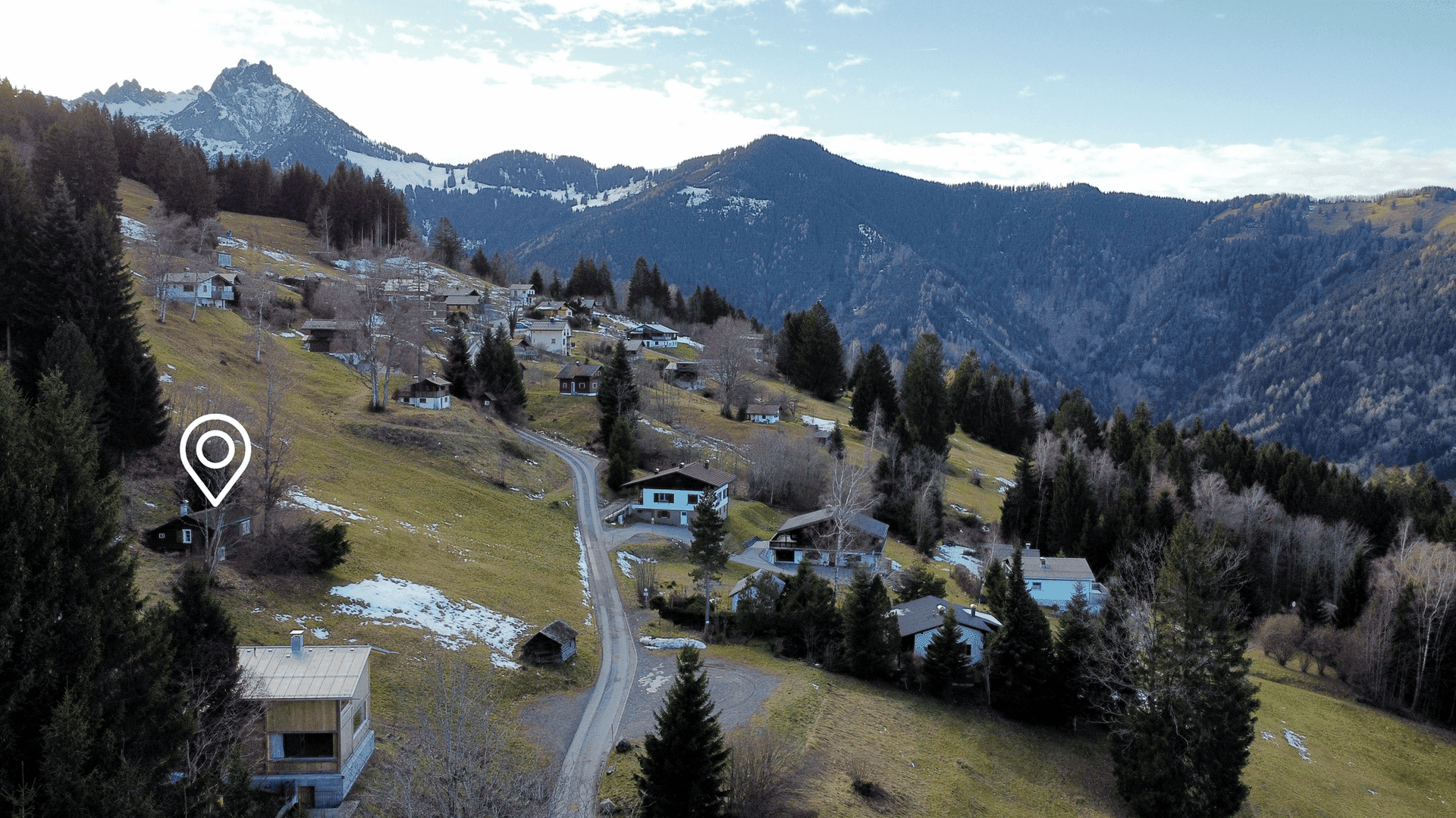 Panoramablick auf ein Bergdorf in einer bewaldeten Landschaft mit schneebedeckten Gipfeln.