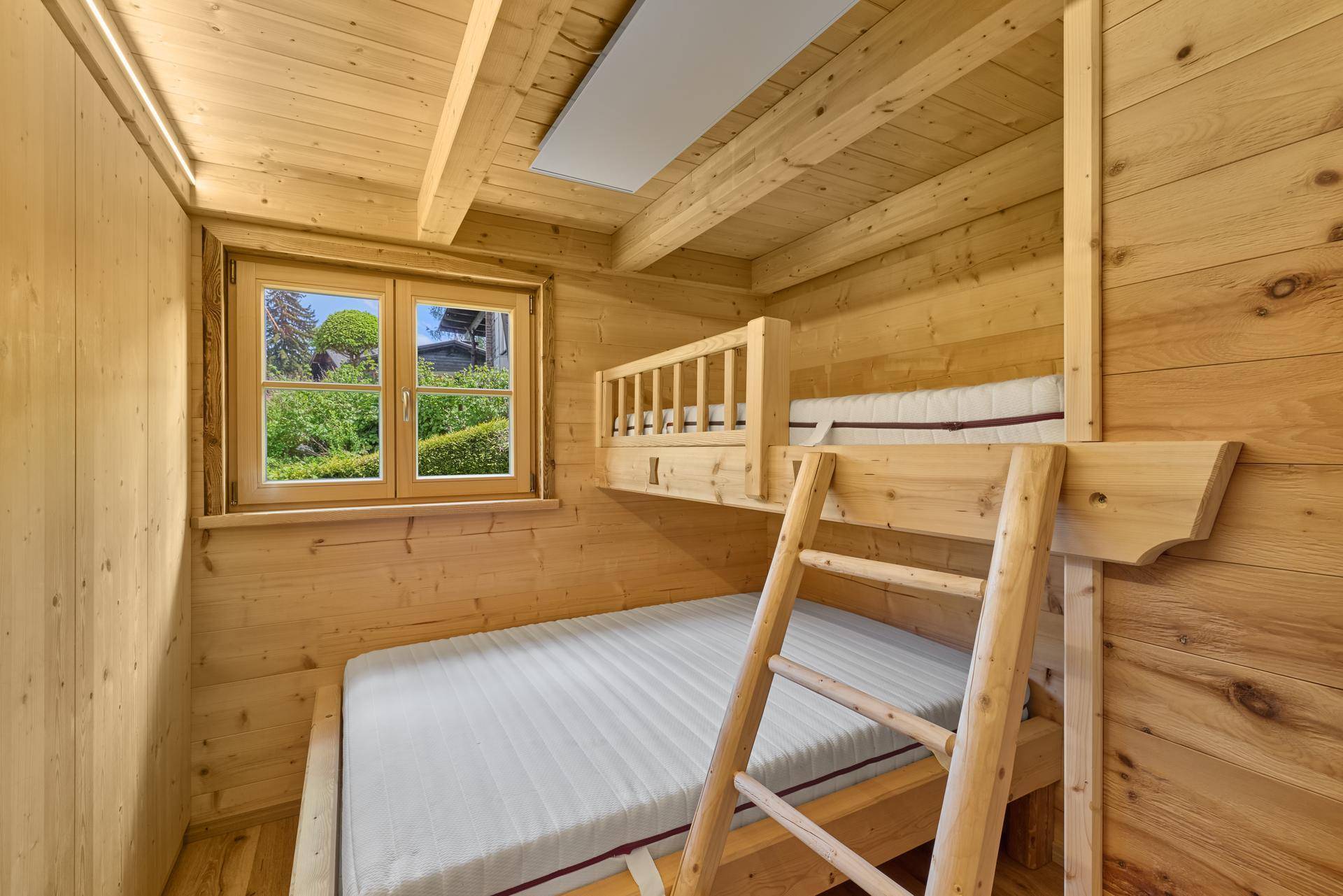 Kinderzimmer in einem Holzchalet mit Etagenbett, Holzwänden und Fensterblick.
