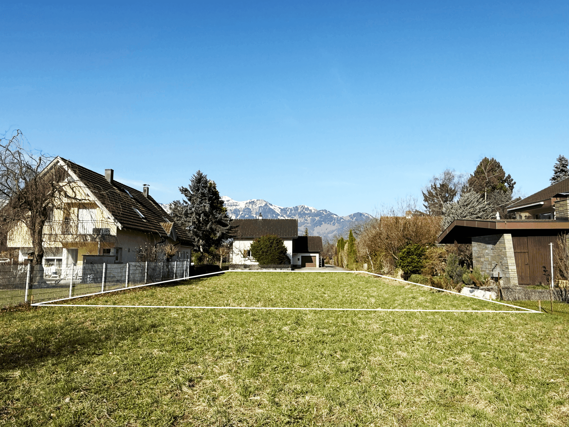 Sonnenbeschienenes Grundstück mit grüner Wiese und Blick auf die umliegende Berglandschaft.
