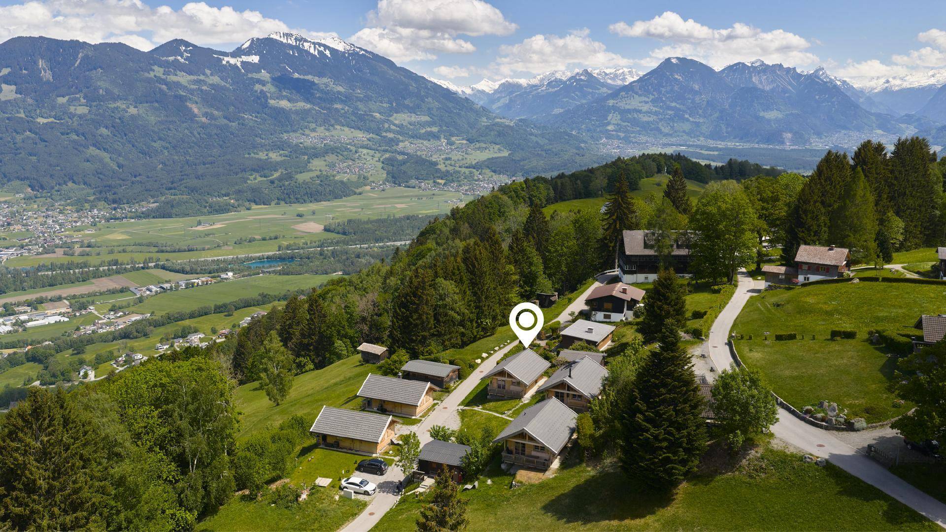 Panoramablick auf eine Chalet-Siedlung in einer weiten Berglandschaft.