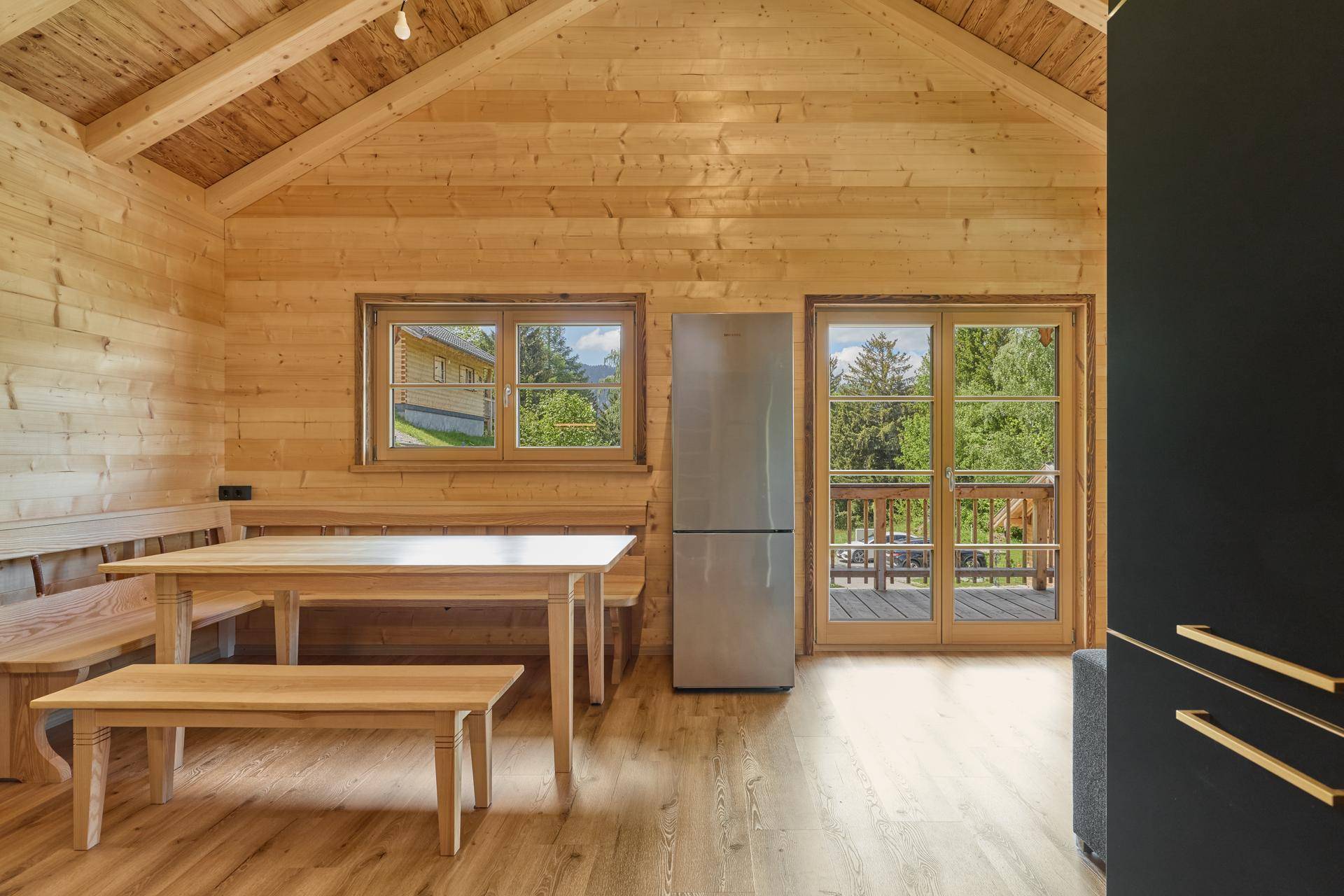 Essbereich in einem Holzchalet mit Holztisch, Bänken und Zugang zum Balkon.