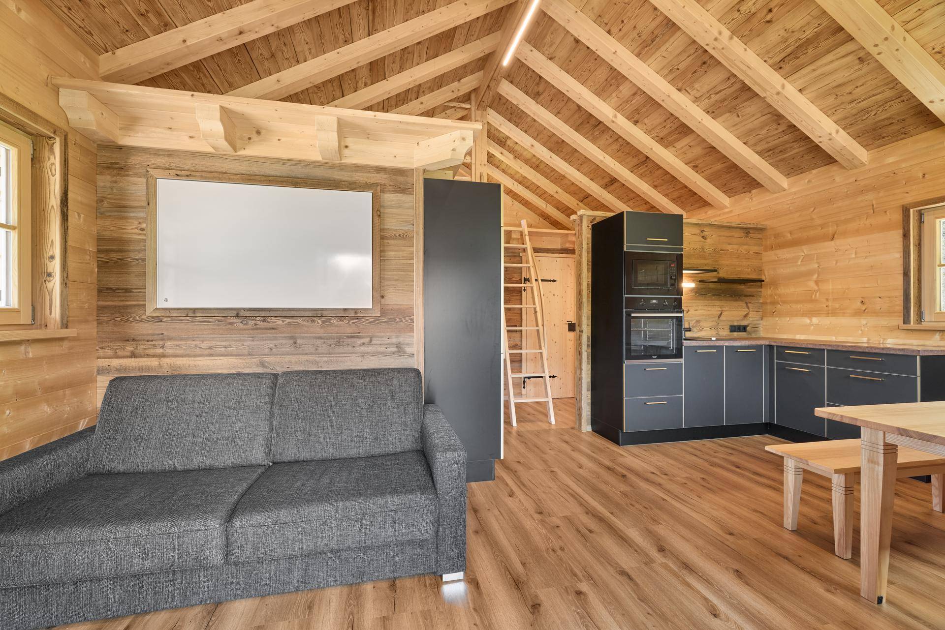 Gemütlicher Wohnbereich in einem Holzchalet mit Sofa, Holzbalkendecke und offener Küche.
