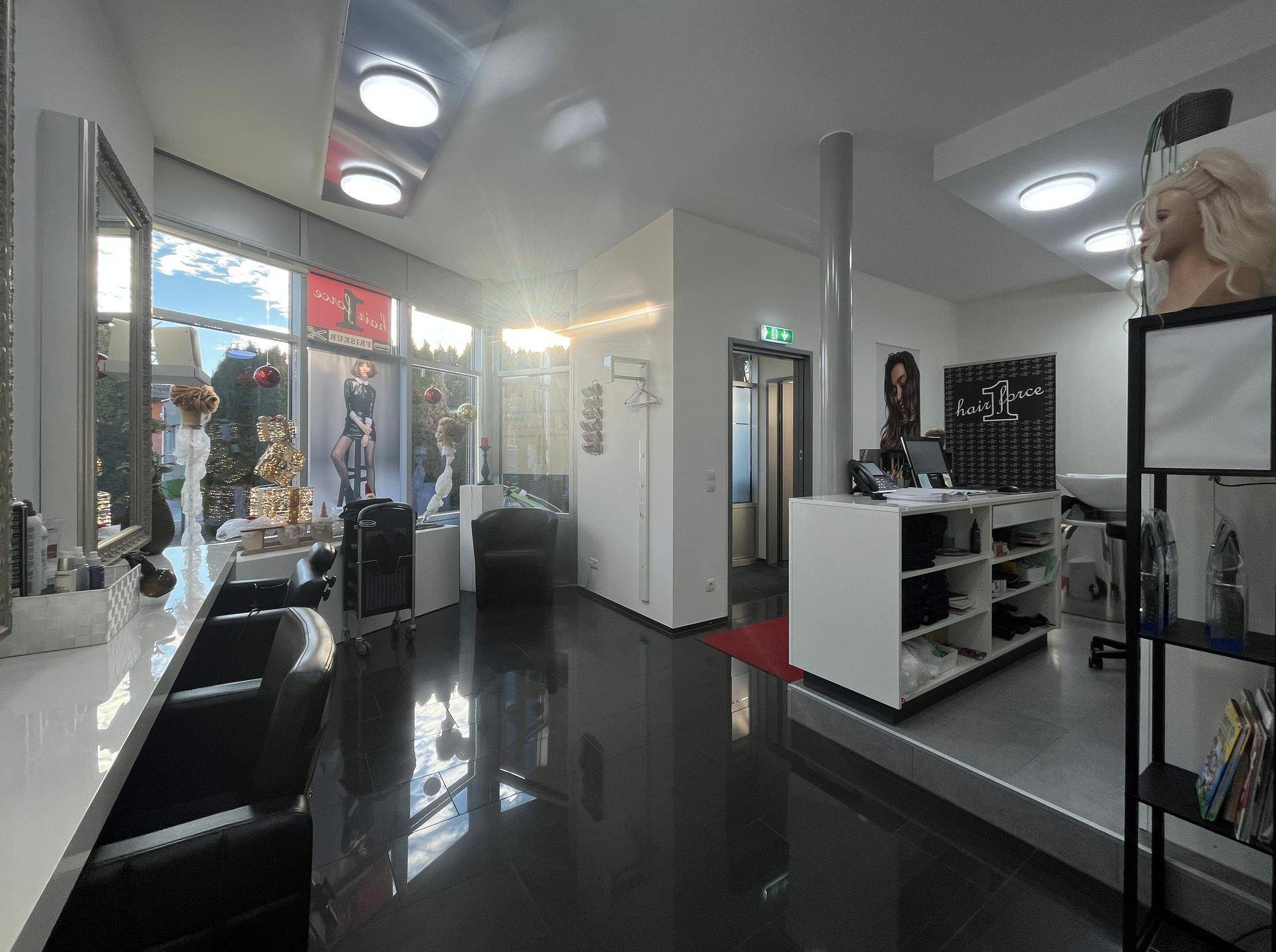 Moderner Geschäftsraum mit Friseurstühlen, Rezeption und großen Schaufenstern für Kunden.